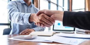 Two businessmen shaking hands in front of a desk.
