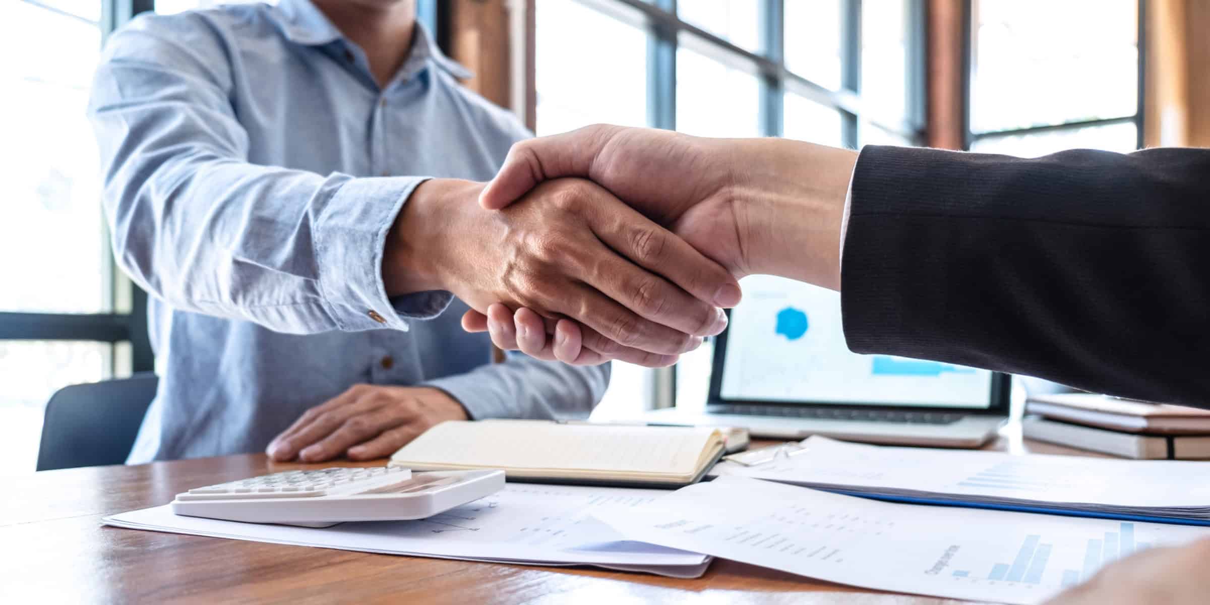 Two businessmen shaking hands in front of a desk.