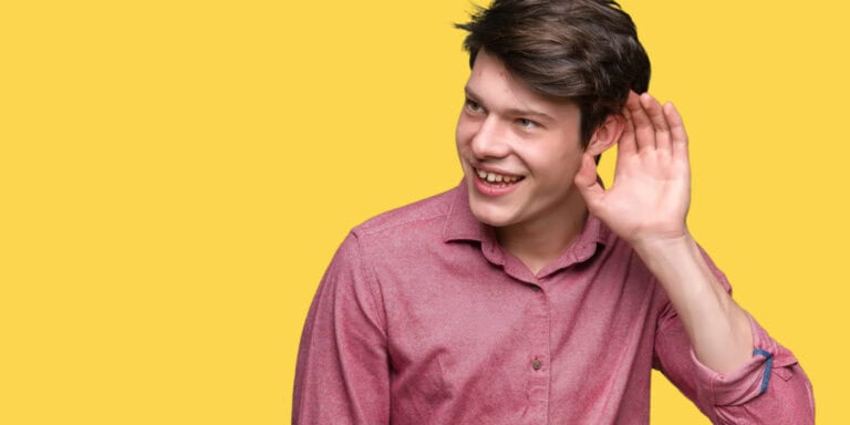 A young man is holding his hand up to his ear.