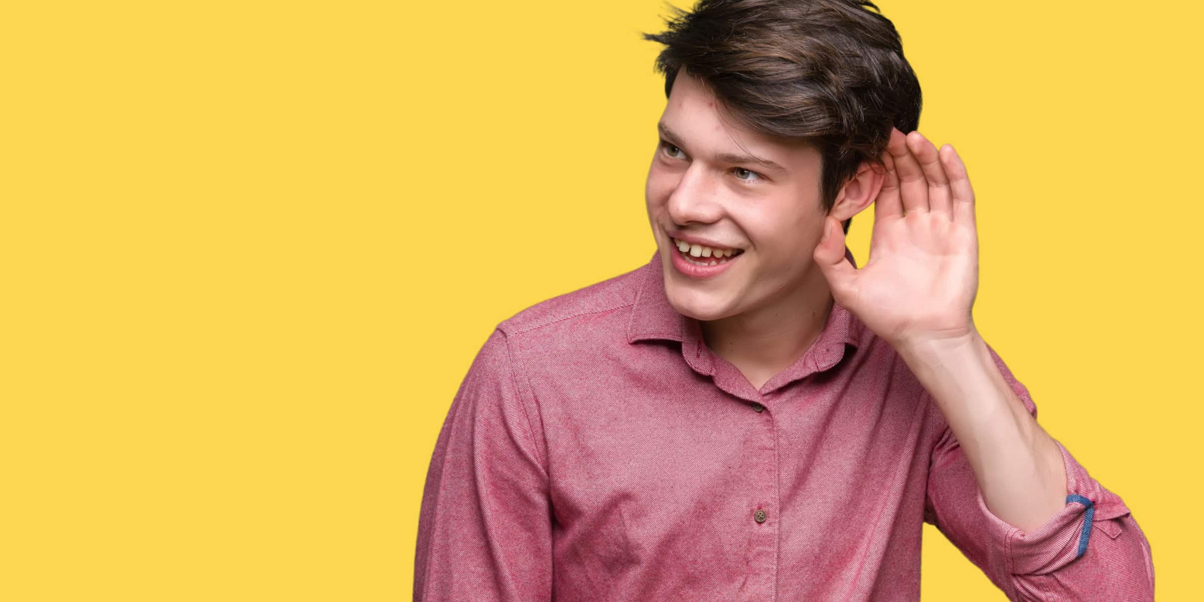 A young man is holding his hand up to his ear.