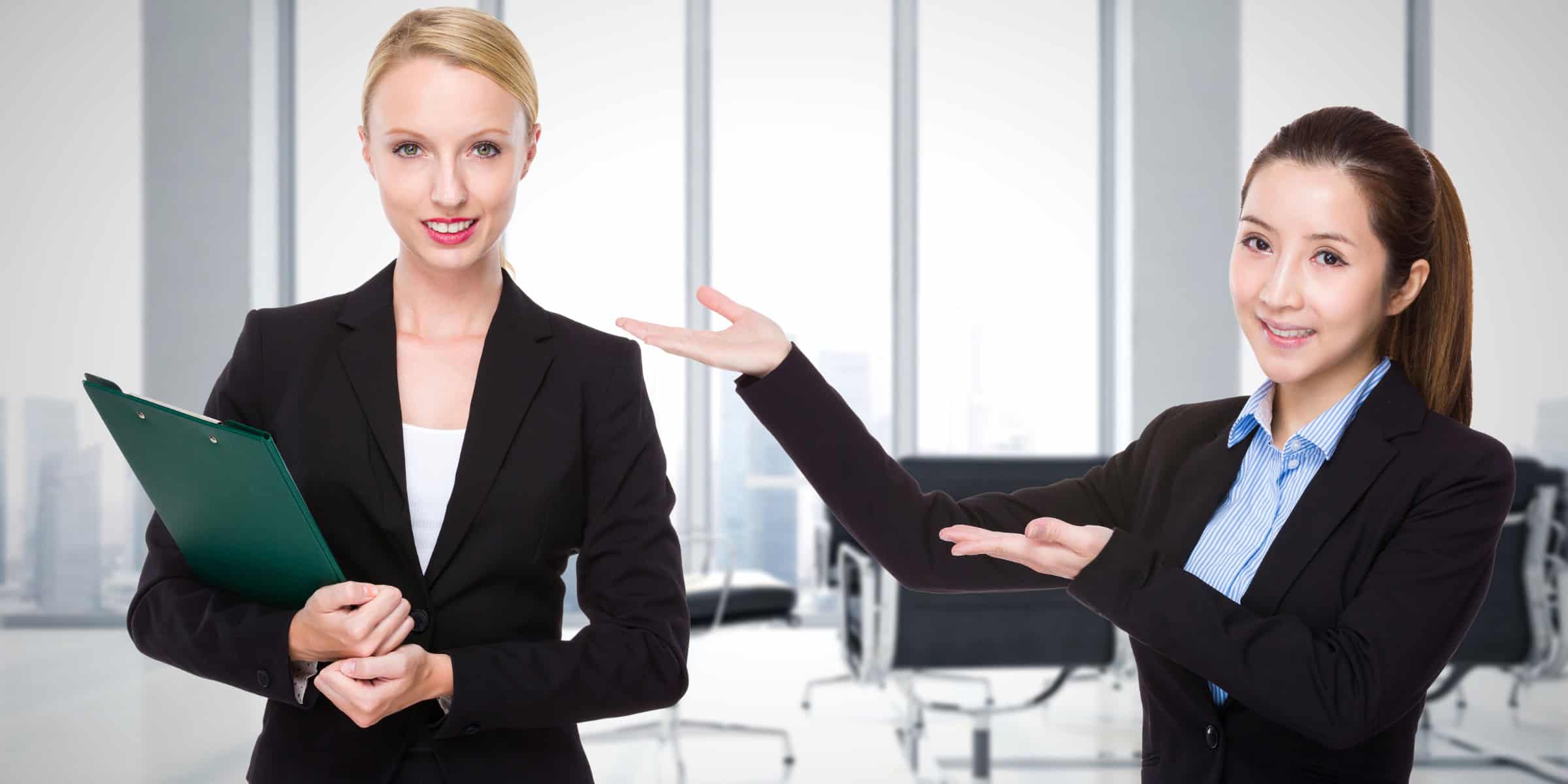 Two women in business suits pointing at each other.