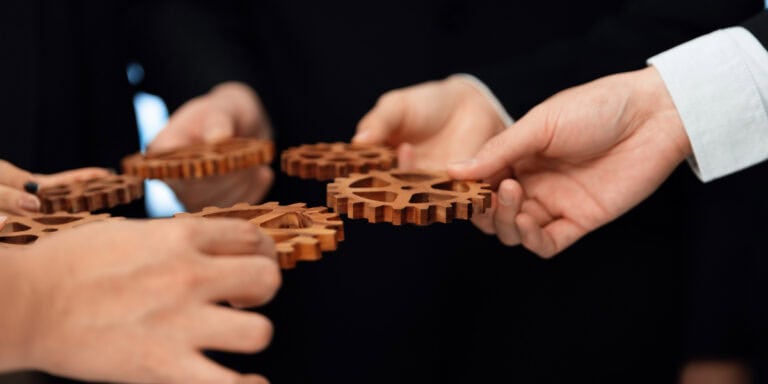 A group of business people holding wooden gears together.