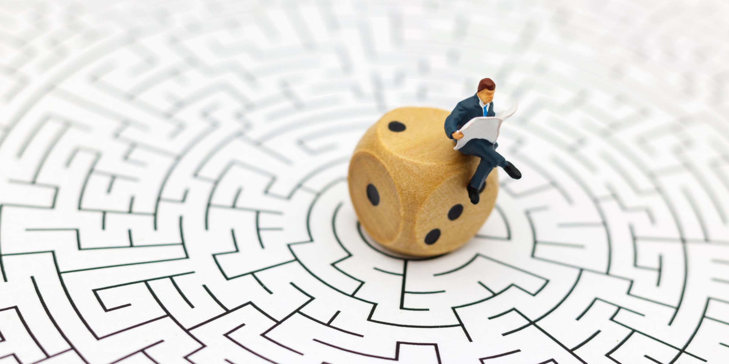 A businessman sitting on a dice in a maze.