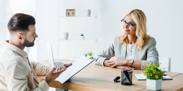 A woman is talking to a man at a table in an office.