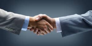 Two businessmen shaking hands on a dark background.