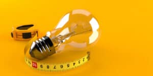 A light bulb next to a measuring tape on a yellow background.