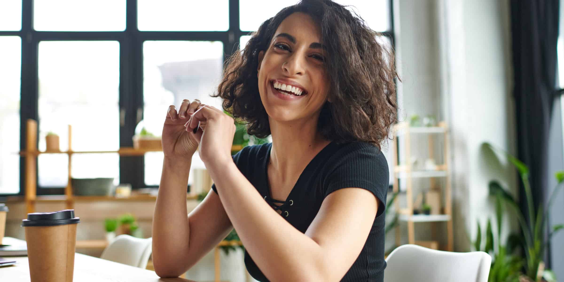 A smiling woman sitting at a desk with a cup of coffee.