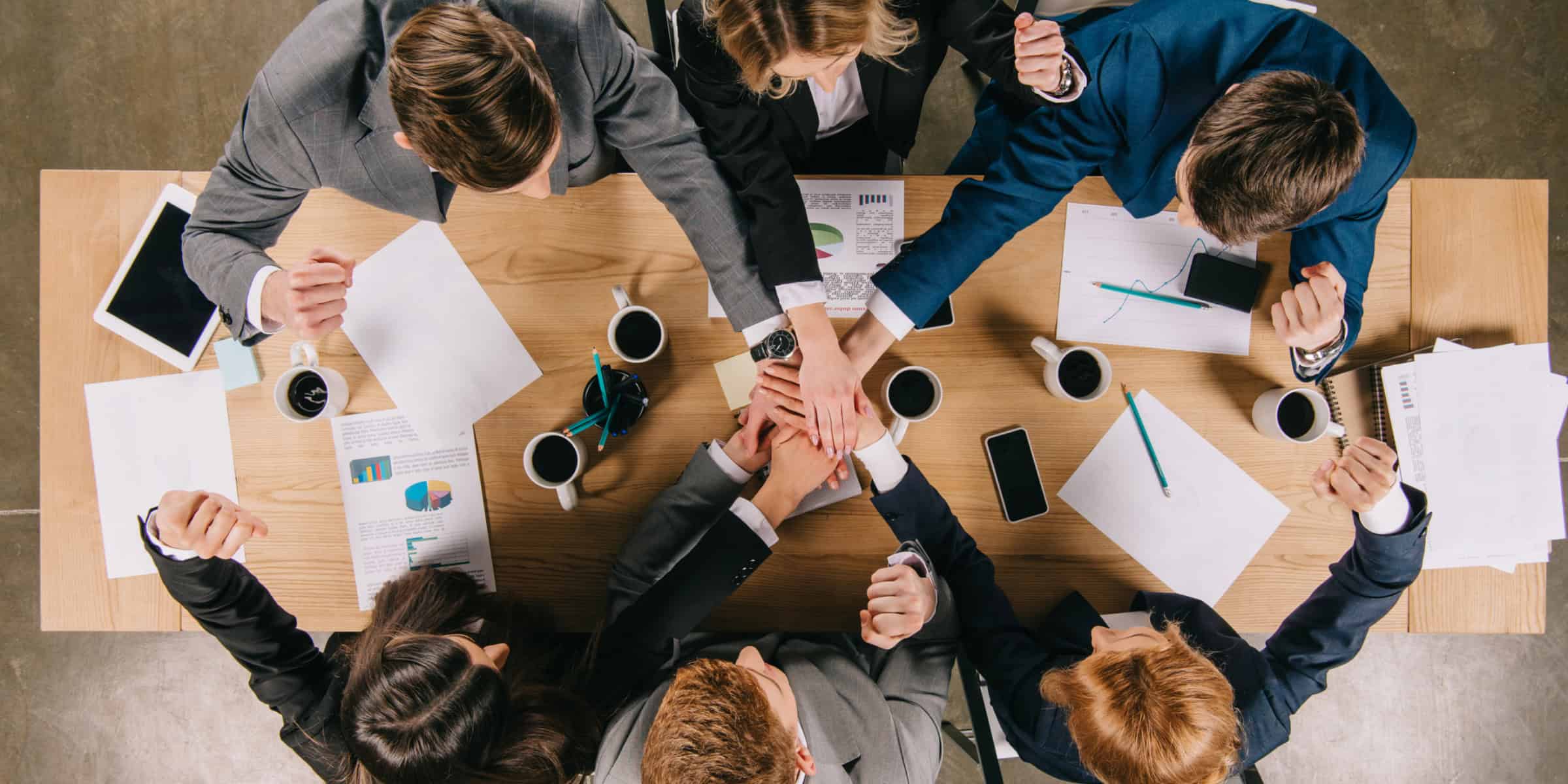 A group of business people holding hands around a table.