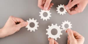 A group of hands holding gears on a gray background.