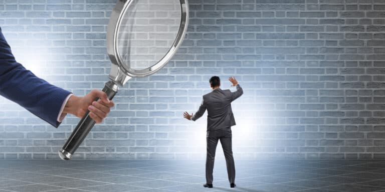 Businessman holding a magnifying glass in front of a brick wall.