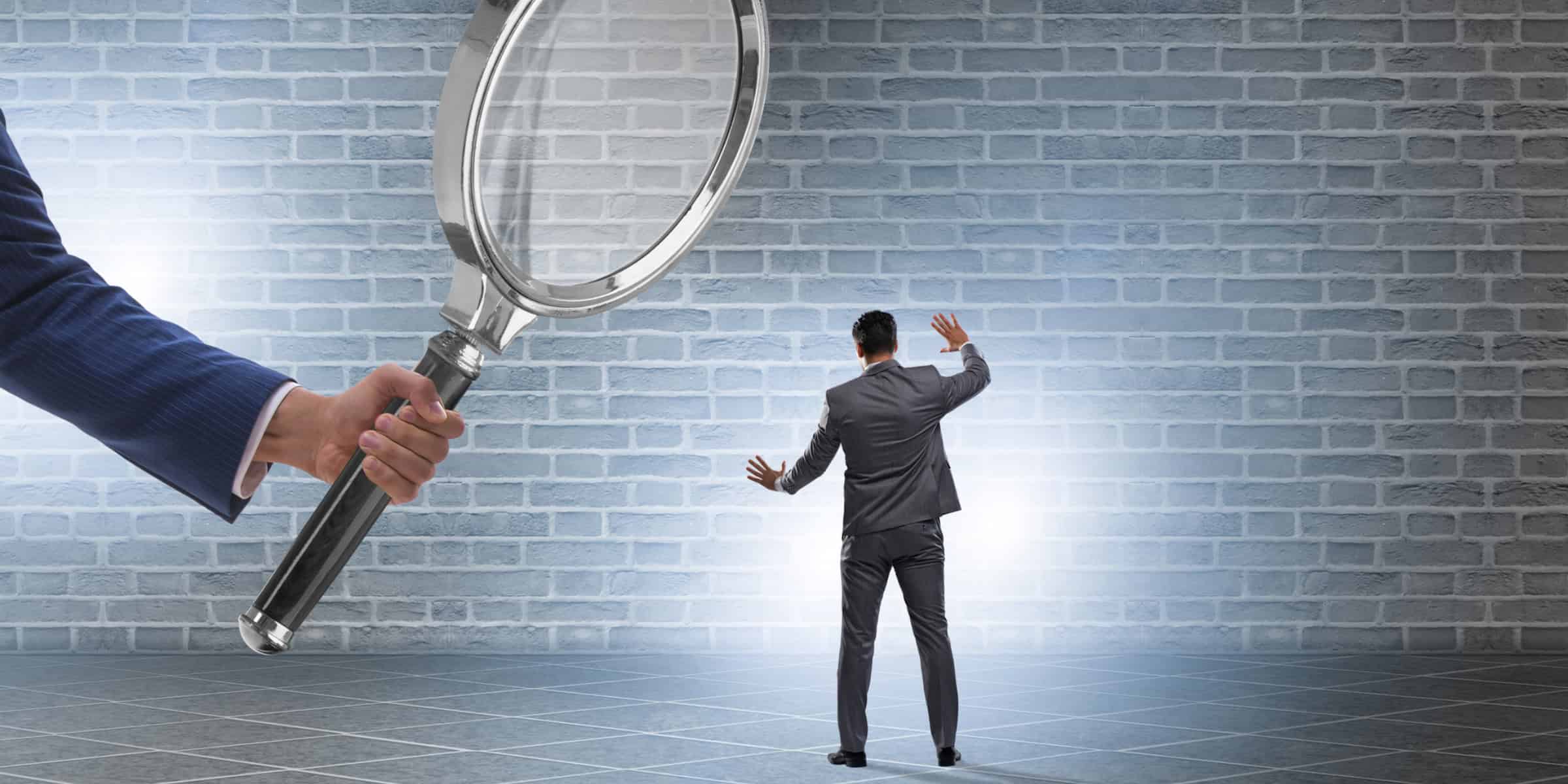 Businessman holding a magnifying glass in front of a brick wall.
