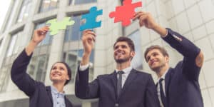 Three business people holding up puzzle pieces in front of a building.