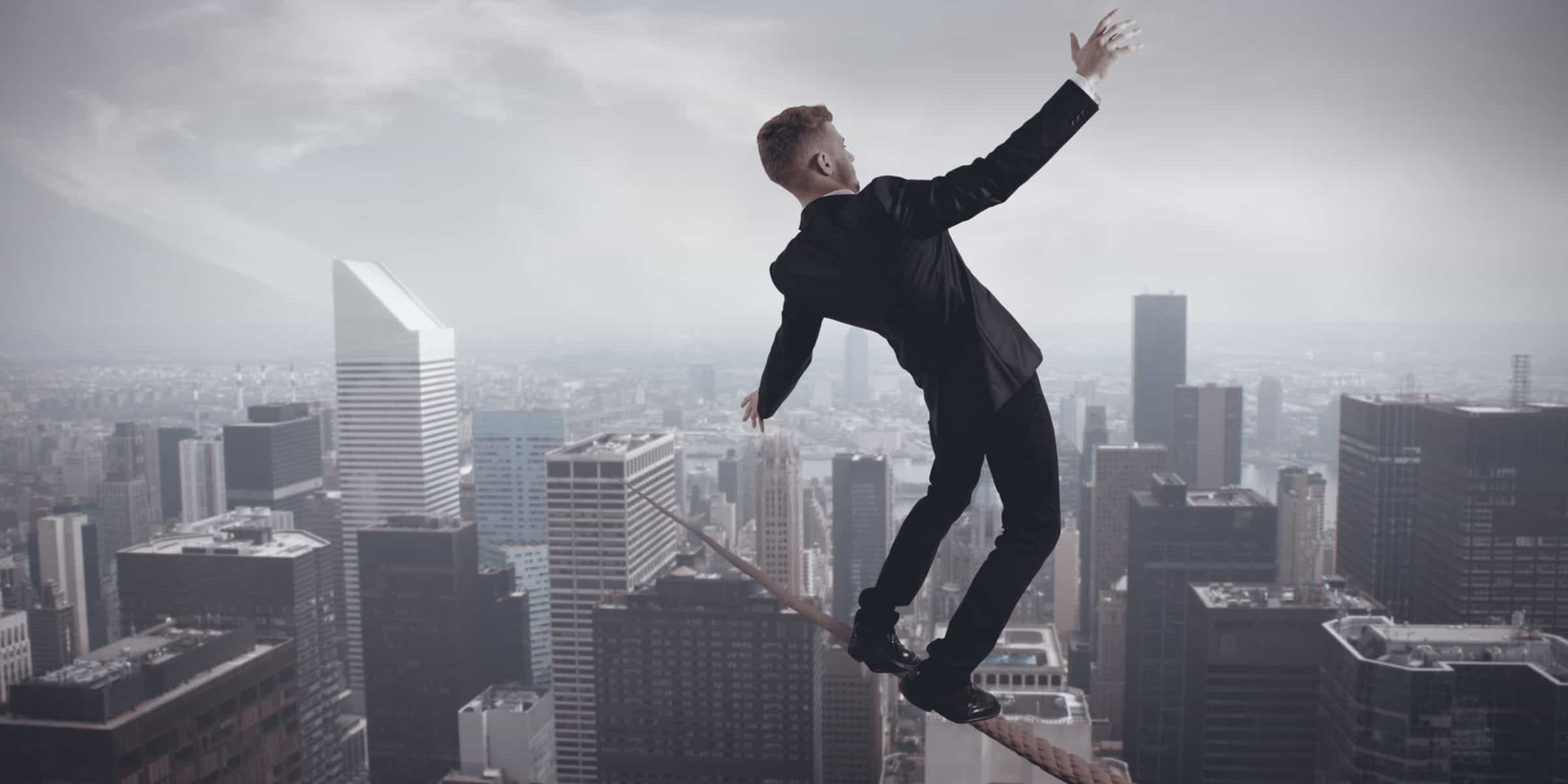 Businessman balancing on a tightrope over a city.