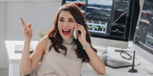 A woman is talking on the phone while sitting in front of several monitors.