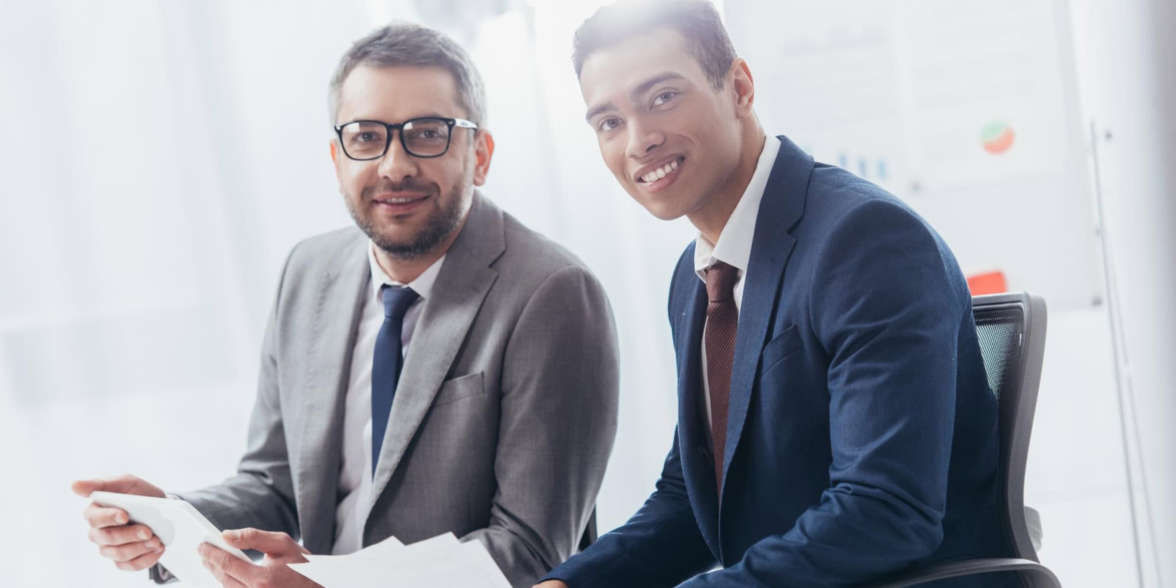 Two businessmen sitting at a desk and looking at papers.