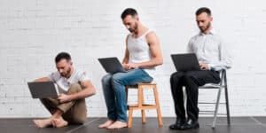 Three men sitting on a chair and using laptops.