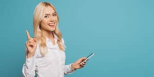 A young woman holding a smart phone and pointing at it.