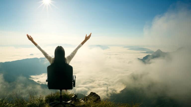 A woman in a wheelchair on top of a mountain with her arms outstretched.