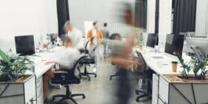 A blurry image of people working at desks in an office.