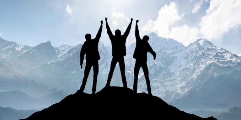 Three people standing on top of a mountain with their arms raised.
