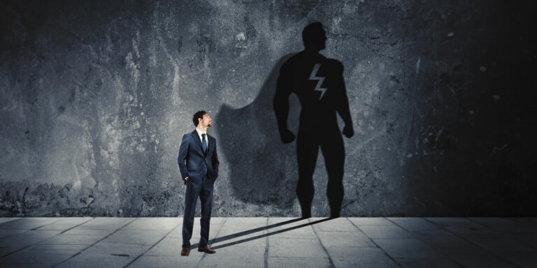 A businessman standing next to a shadow of a superhero.