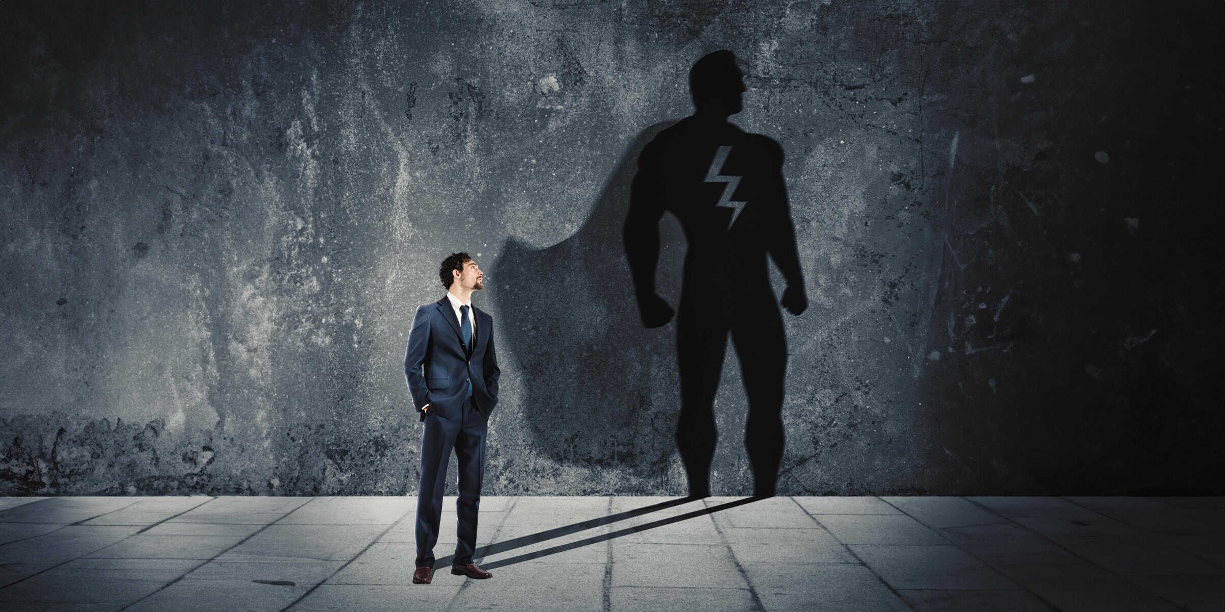A businessman standing next to a shadow of a superhero.