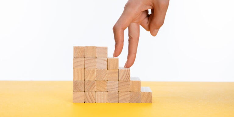 A woman's hand reaching up to a stack of wooden blocks.