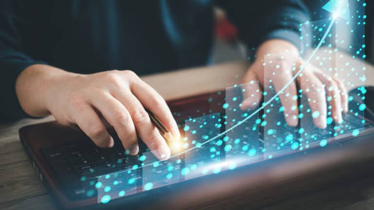 A person typing on a laptop with a graph on it.