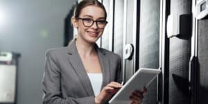A woman in glasses is holding a tablet in a server room.