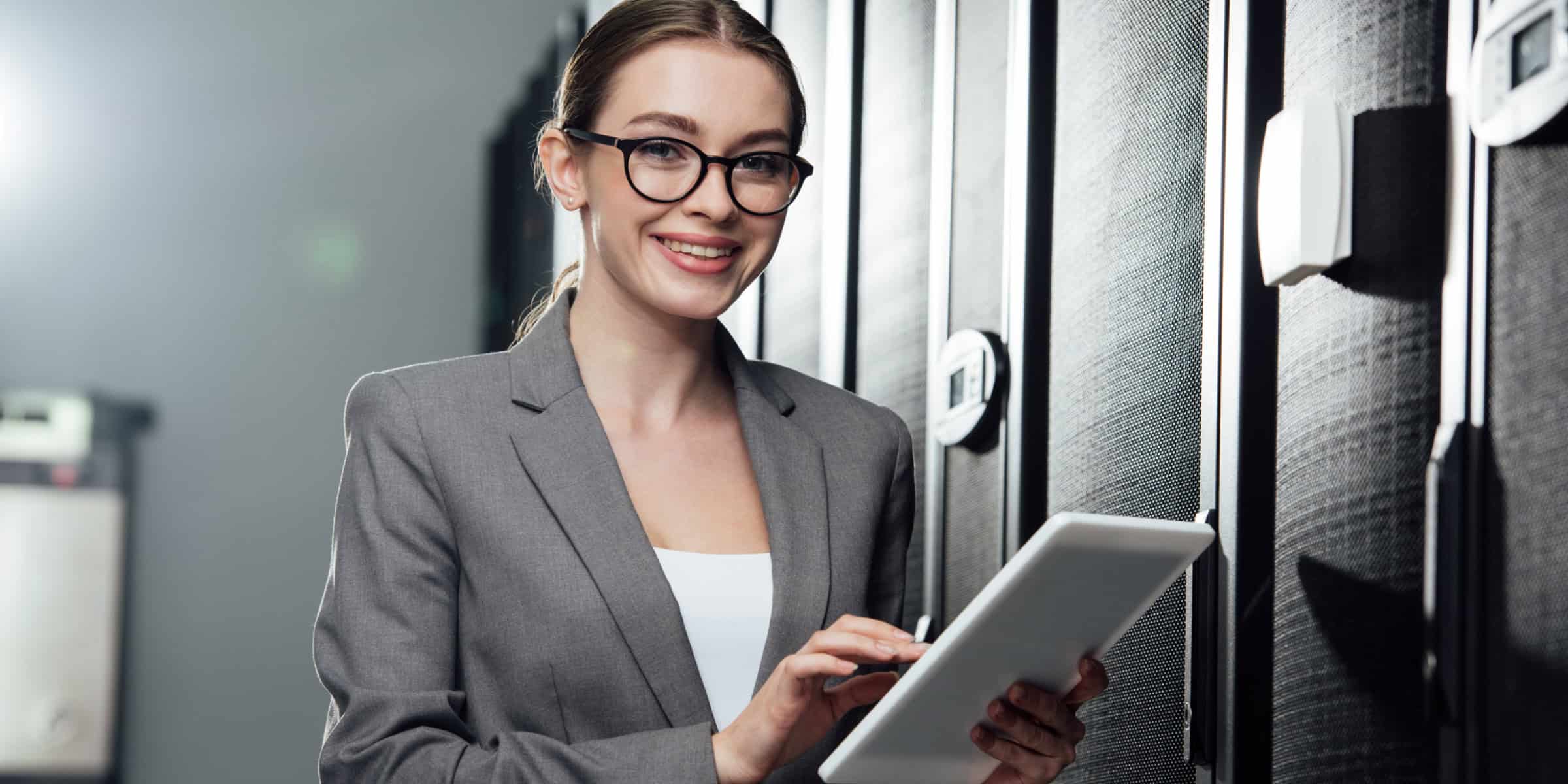 A woman in glasses is holding a tablet in a server room.