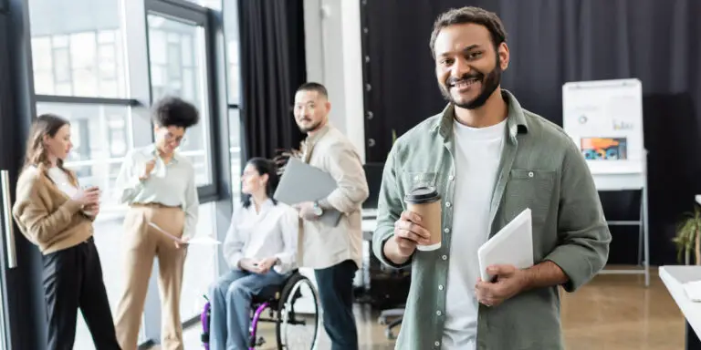 A group of people in an office with a man holding a cup of coffee.