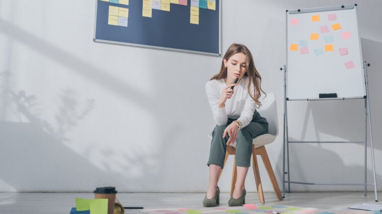 A woman sitting on a chair in front of a whiteboard with sticky notes on it.