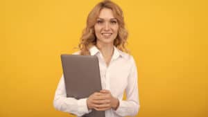 A young woman holding a laptop on a yellow background.