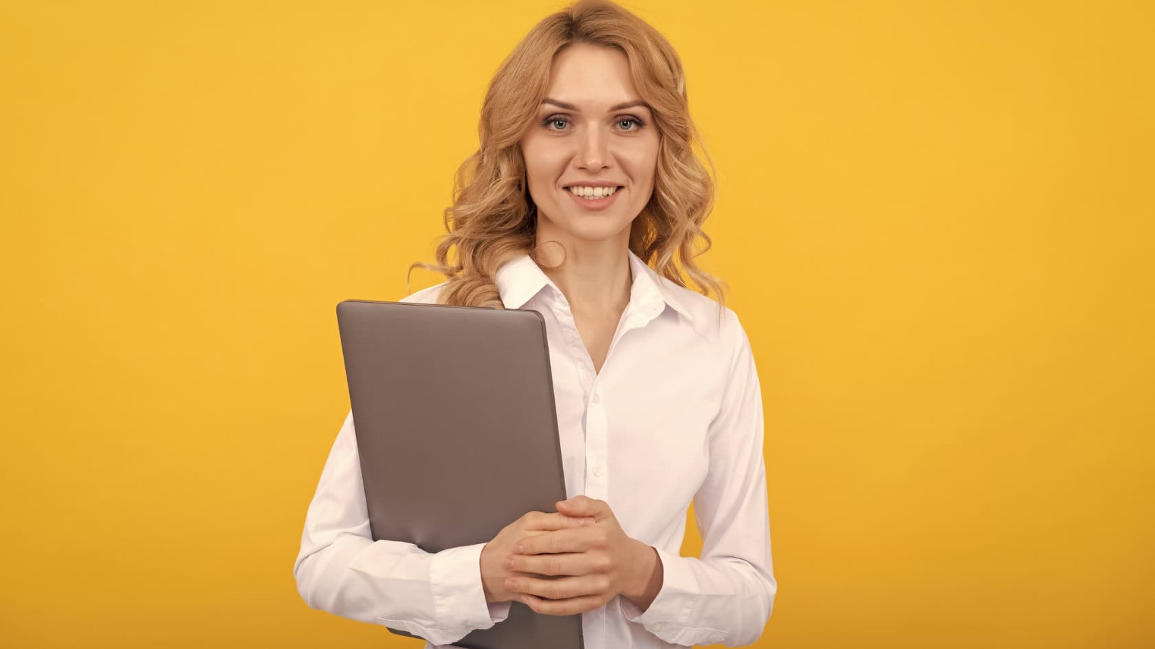 A young woman holding a laptop on a yellow background.