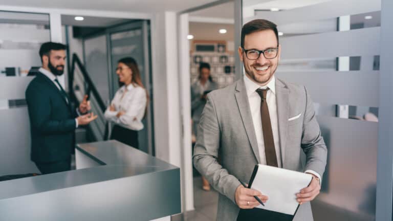 A businessman holding a clipboard in an office.