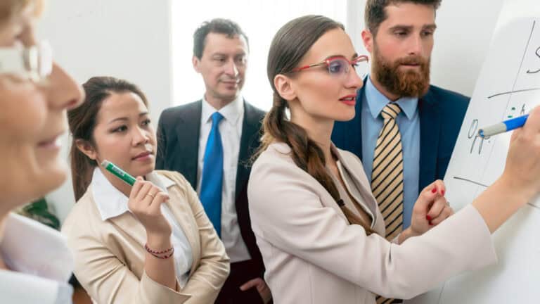 A group of business people working together on a whiteboard.