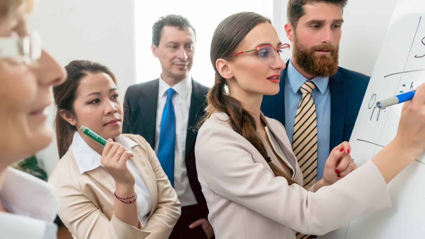 A group of business people working together on a whiteboard.