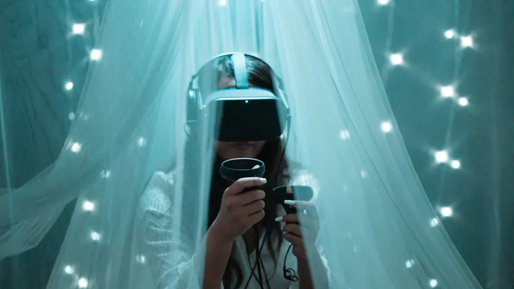 Person using a VR headset and controllers under sheer curtains with string lights in the background.